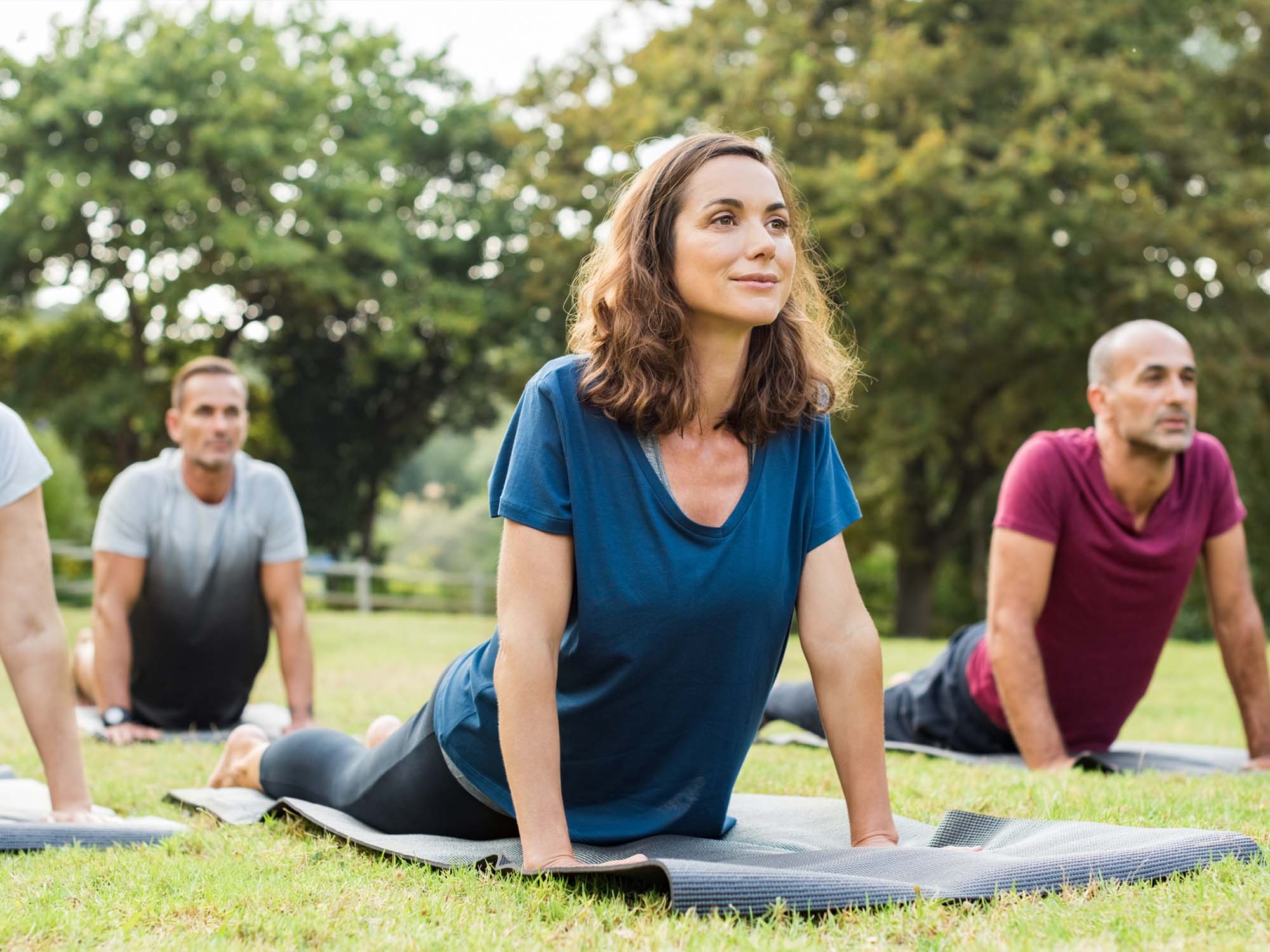 Foto: iStock / Ridofranz; Frauen und Männer machen Yoga auf einer Matte im Park